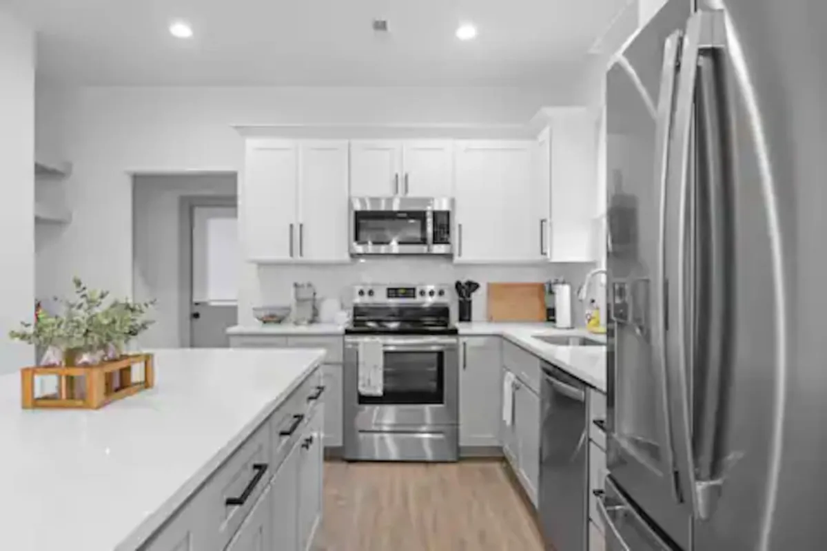 A modern kitchen with shining stainless steel appliances, a large kitchen island for meal prep or casual dining, and crisp white cabinetry. The design is open and conducive to both family meals and entertaining guests, reflecting a contemporary yet comfortable style.