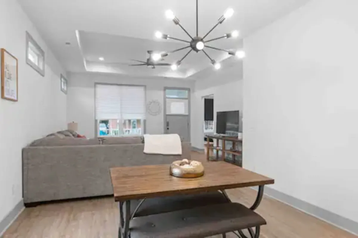 An inviting living and dining area with a wooden table set for meals and a plush, comfortable sofa ideal for relaxing. The modern light fixture overhead and the television unit create a casual, welcoming space designed for entertaining, collaborating, or simply unwinding.