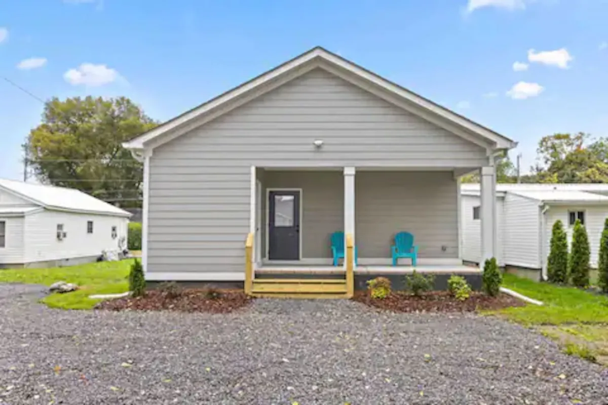 A welcoming front porch scene with blue chairs and a landscaped garden, bathed in warm natural light. The setting evokes quiet mornings or unwinding in the evening, bridging the experience of busy downtown life with at-home comfort and privacy.