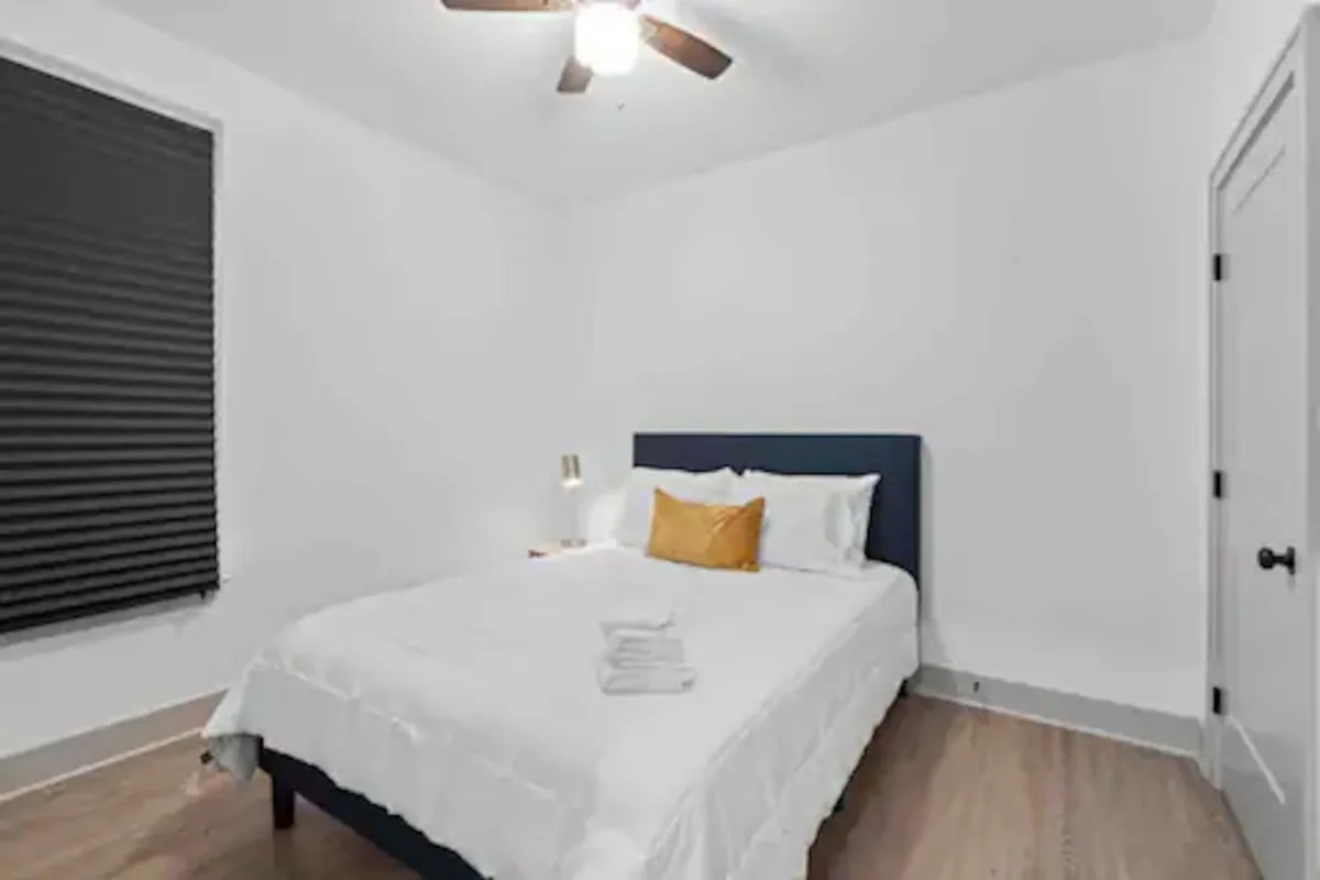 A cozy, peaceful bedroom with a comfortable bed, a decorative pillow, a nightstand, and a soft lamp. Gentle natural light filters through the blinds, creating an inviting environment conducive to relaxation or reading before sleep.