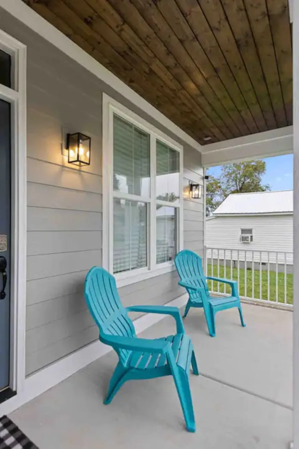 This image showcases the home's welcoming exterior, featuring turquoise chairs on the front porch, a front door, a window with blinds, and decorative lanterns. The scene evokes a sense of relaxation and community, suggesting a pleasant environment to return to after work or a space to connect with neighbors.