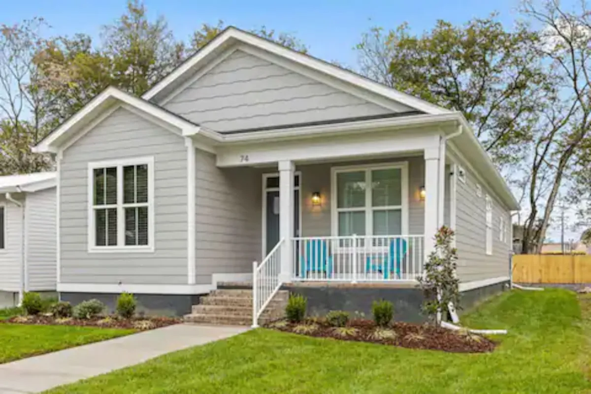 A charming exterior shot of the home's front porch, featuring inviting blue chairs and well-maintained landscaping. The scene is lively and welcoming, suggesting a place to relax or socialize after enjoying city life, with the porch connecting directly to the home's entrance.